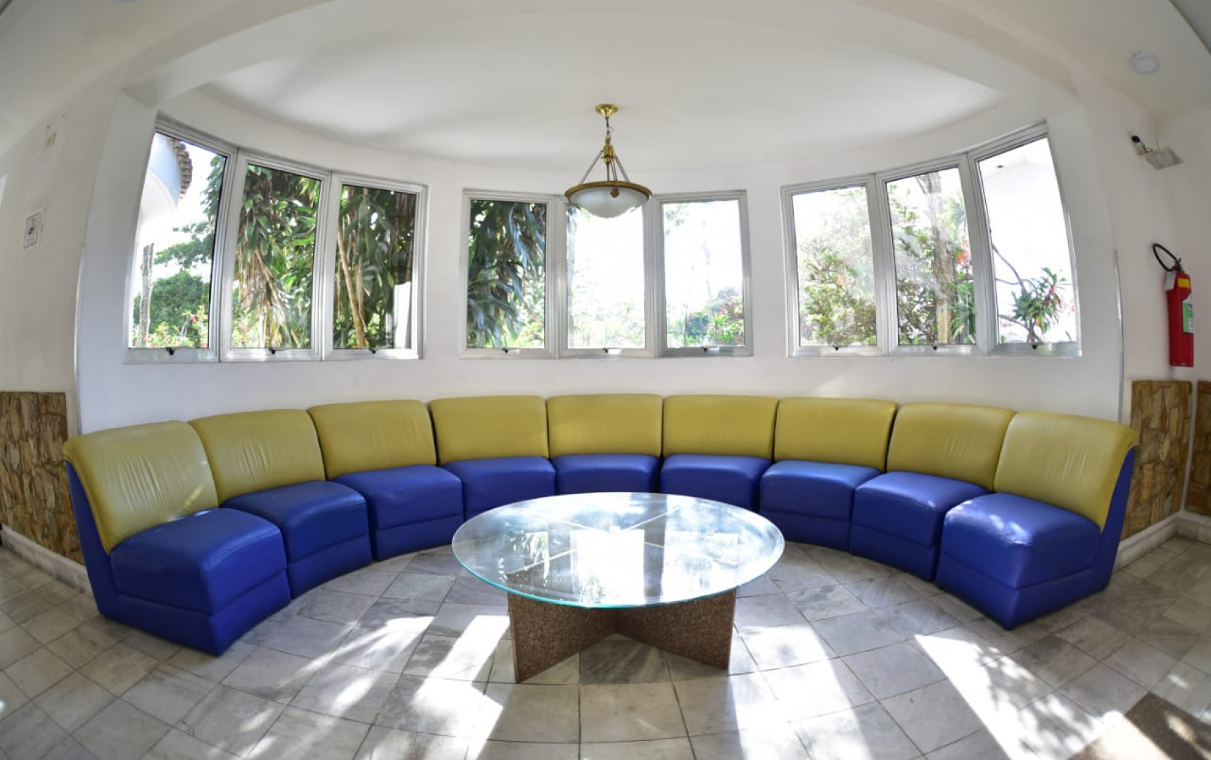 Sala de estar circular envidraçada, com sofá contínuo e vista para as árvores